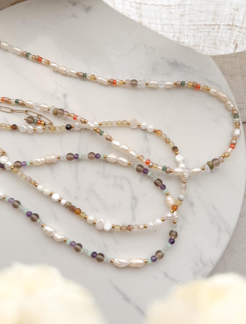 May include: Three layered necklaces with white pearls and various colored beads, including green, brown, orange, and purple.