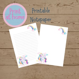 Puede incluir: Papel para cartas imprimible con un unicornio, un arcoíris y nubes. El texto "Imprime en casa" y "Papel para cartas imprimible" está incluido en la imagen.