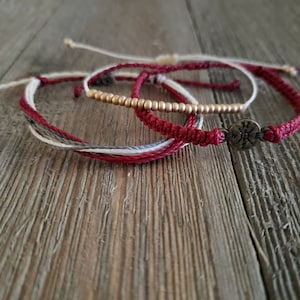 May include: Three bracelets, one with a compass charm, one with gold beads, and one with red, white, and gray threads.