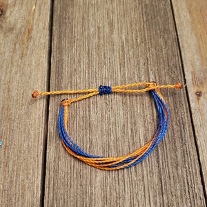 May include: A blue and orange braided friendship bracelet. The bracelet is tied with a knot and is ready to be worn.