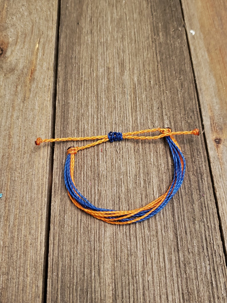 May include: A blue and orange braided friendship bracelet. The bracelet is tied with a knot and is ready to be worn.