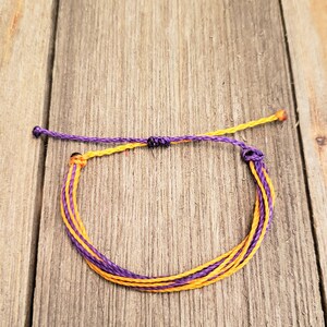 May include: A purple and orange friendship bracelet made of braided string.