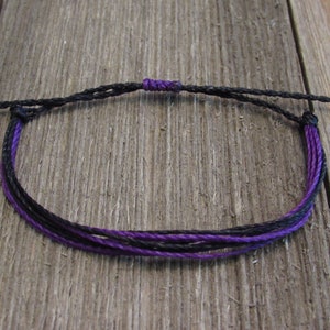 May include: A black and purple braided bracelet with adjustable knot closure.