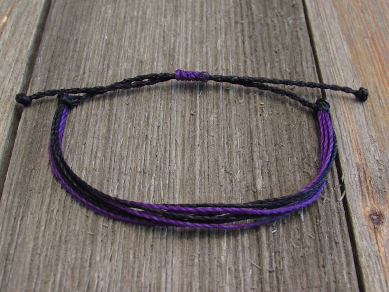 May include: A black and purple braided bracelet with adjustable knot closure.
