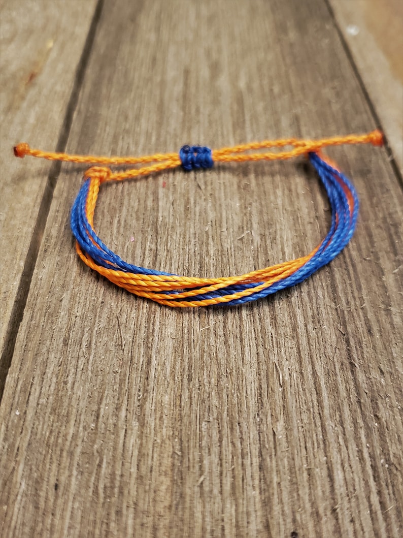May include: A blue and orange friendship bracelet made of woven string. The bracelet is tied with a knot at the end.