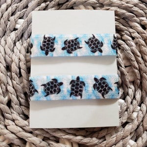 May include: Two blue and white tie-dye hair scrunchies with black turtle designs.