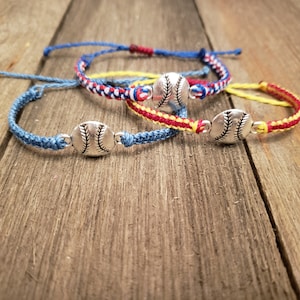 May include: Three friendship bracelets with baseball charms. The bracelets are blue, red and white, and yellow and red.