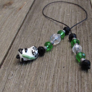 May include: A black and white panda charm with green bamboo hanging from a black cord with green, clear, and black beads.