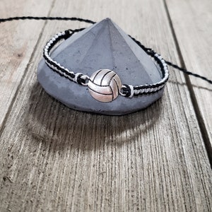 May include: Black and white braided bracelet with a silver volleyball charm.
