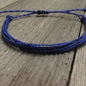 May include: A navy blue braided cord bracelet with a simple knot closure.