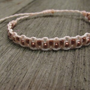 May include: A delicate pink and copper beaded bracelet with a simple knot closure.
