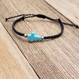 May include: A black braided cord bracelet with a turquoise blue cross charm and silver beads.