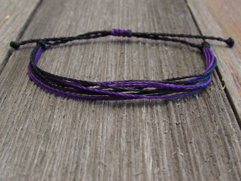 May include: A simple bracelet made of black and purple cord. The bracelet is tied with a knot at the end.