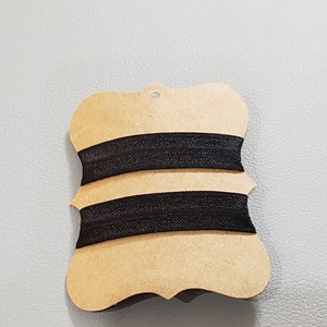 May include: Two black elastic bands wrapped around a brown card with a decorative edge.