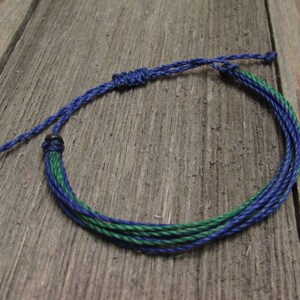 May include: A blue and green braided friendship bracelet with a knot closure.
