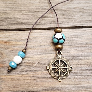 May include: A brown string bookmark with a compass charm and turquoise and white beads.
