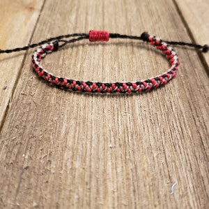May include: A red, black, and gray braided friendship bracelet with a red knot closure.