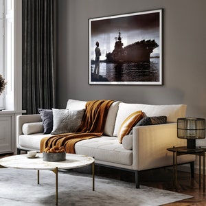 May include: A white sofa with a brown throw blanket and pillows, a black and gold side table with a lamp, and a coffee table with a bowl of oranges. A framed black and white photo of a ship hangs on the wall.