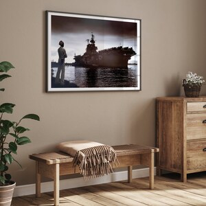 May include: A framed black and white photograph of a large ship docked at a pier. A person stands on the pier looking out at the ship.