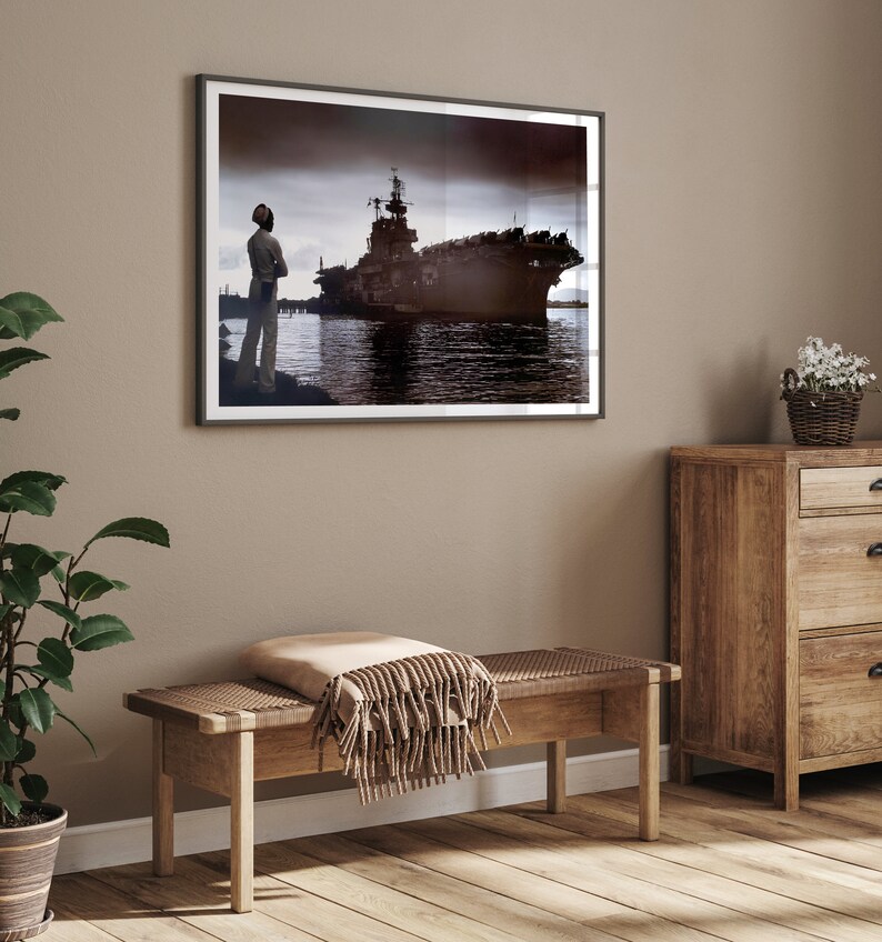 May include: A framed black and white photograph of a large ship docked at a pier. A person stands on the pier looking out at the ship.