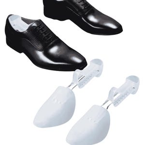 Könnte beinhalten: Schwarze Lederschuhe mit Schnürsenkeln, zusammen mit zwei weißen Schuhspannern. Die Schuhe haben eine glänzende Oberfläche und ein klassisches Design. Die Schuhspanner sind aus Kunststoff und halten die Form der Schuhe.