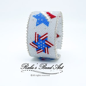 May include: A white beaded bracelet with red, white, and blue stars. The bracelet is made with small beads and has a silver clasp. "Ralu's Bead Art" is written on the bottom of the image.