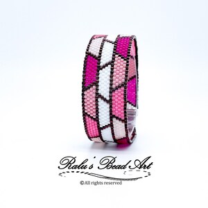 May include: A pink, white, and brown beaded bracelet with a geometric pattern. The bracelet is made of small, square beads that are arranged in a repeating pattern of triangles. The bracelet is shown on a white background.