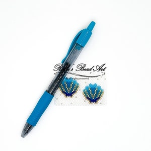 Op de afbeelding: Een paar blauwe en gouden kralen oorbellen in de vorm van schelpen. De oorbellen zijn op een witte achtergrond met een pen voor schaal.