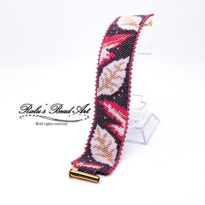 May include: A beaded bracelet with a pink, gold, and black leaf pattern. The bracelet has a gold clasp.