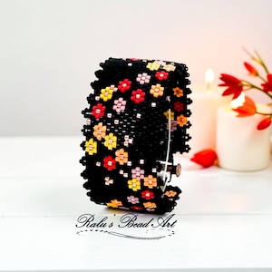 May include: Black beaded cuff bracelet featuring a floral design in red, yellow, and pink. The bracelet has a clasp closure. The text "Ralu's Bead Art" is visible at the bottom.