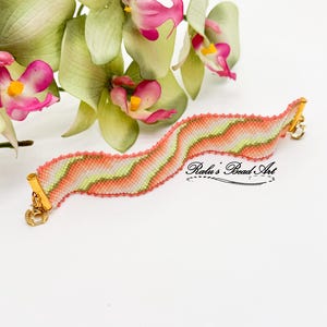 May include: A pink, green and white beaded bracelet with a gold clasp. The bracelet is woven in a chevron pattern. The bracelet is photographed against a white background with a green orchid.