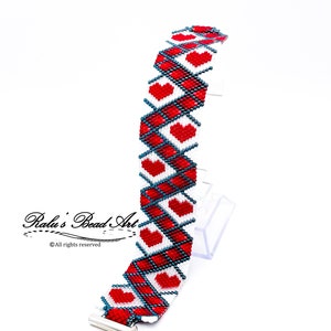 May include: A red and white beaded bracelet with a heart pattern. The bracelet has a silver clasp and is made with small, round beads.