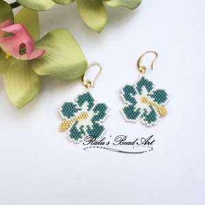 Può includere: Un paio di orecchini a fiori fatti a mano con perline. Gli orecchini presentano una combinazione di colori verde acqua, bianco e oro. Il design floreale è dettagliato con piccole perline e gli orecchini hanno ganci dorati. Sfondo bianco.