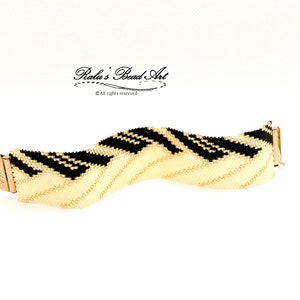 Peut inclure: Un bracelet en perles noires et crème avec un motif ondulé. Le bracelet est fait de petites perles et a un fermoir doré. Le bracelet est sur un fond blanc. "Ralu's Bead Art" est écrit en cursive noire sur un fond blanc.