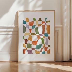 Pode incluir: Uma impressão de arte abstrata em aquarela emoldurada. A obra apresenta um design geométrico colorido com formas sobrepostas em tons de laranja, verde, amarelo, azul e roxo. A impressão é exibida em uma moldura de madeira marrom claro.