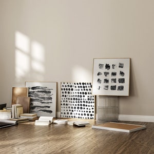May include: A collection of framed black and white abstract art prints with geometric shapes and patterns. The prints are displayed on a white wall with a wooden floor.