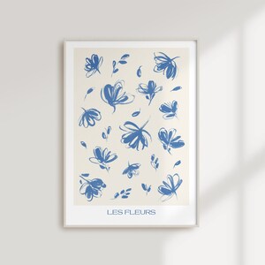 May include: A framed print with a white background and blue abstract floral designs. The text "LES FLEURS" is at the bottom of the print.