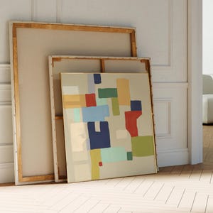 Könnte beinhalten: Abstraktes geometrisches Gemälde mit beigefarbenem Hintergrund und bunten Formen in Rot-, Blau-, Grün- und Gelbtönen. Das Gemälde ist in Gold gerahmt und lehnt an einer weißen Wand.