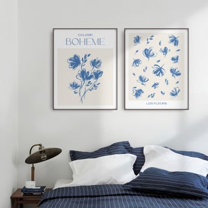 May include: Two framed prints featuring blue floral illustrations. The left print displays the text "Galerie Boheme" and a single bouquet of flowers. The right print displays the text "Les Fleurs" and a pattern of scattered flowers.