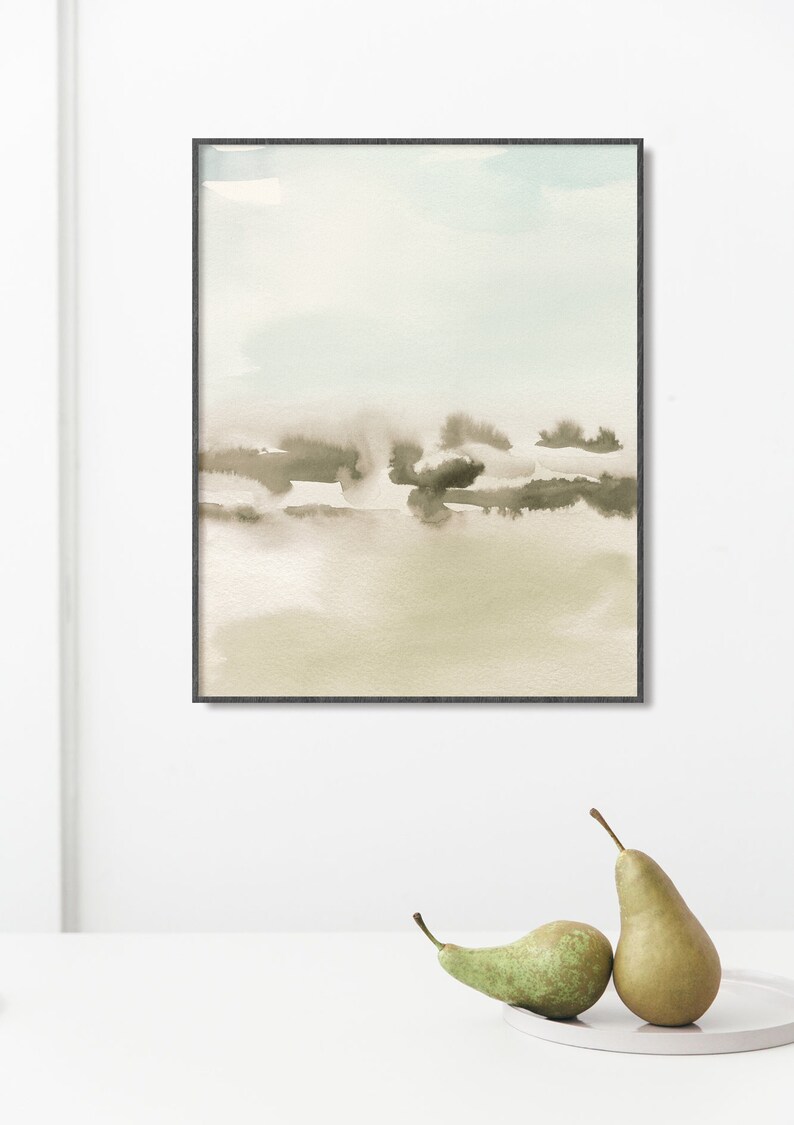 Op de afbeelding: Een ingelijst abstract aquarel schilderij met een lichtblauw, beige en bruin kleurenschema. Het schilderij toont een landschap met een wazige, atmosferische sfeer.