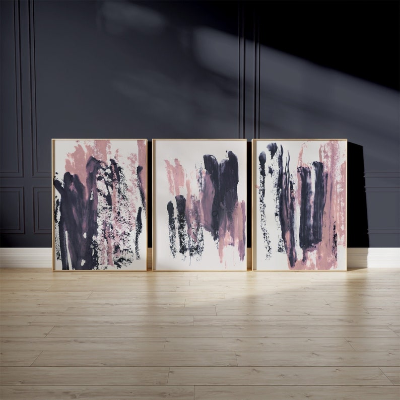 May include: Three abstract paintings with a white background and pink and black brushstrokes. The paintings are framed in gold.