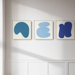 May include: Three framed abstract art prints featuring blue and white shapes. The prints are displayed on a white wall.