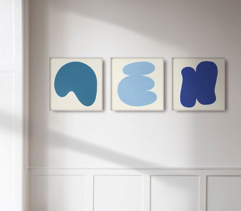 May include: Three framed abstract art prints featuring blue and white shapes. The prints are displayed on a white wall.