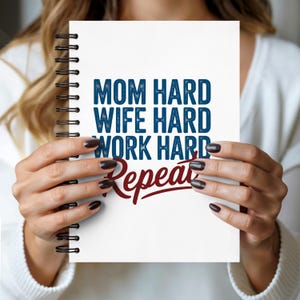 May include: A white spiral-bound notebook with the words "MOM HARD, WIFE HARD, WORK HARD, Repeat" in blue and red lettering. The notebook is held by a person.