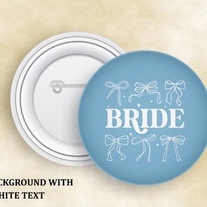 May include: A light blue button with the word "BRIDE" in white, surrounded by white bow illustrations. The button is round and has a white pin backing. The text "BLUE BACKGROUND WITH WHITE TEXT" is at the bottom.