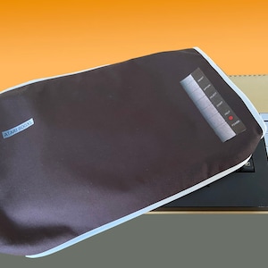 Puede incluir: Una funda de polvo negra con ribete blanco para una computadora Atari 800XL. La funda tiene el texto "ATARI 800XL" impreso en ella. La computadora es visible debajo de la funda.