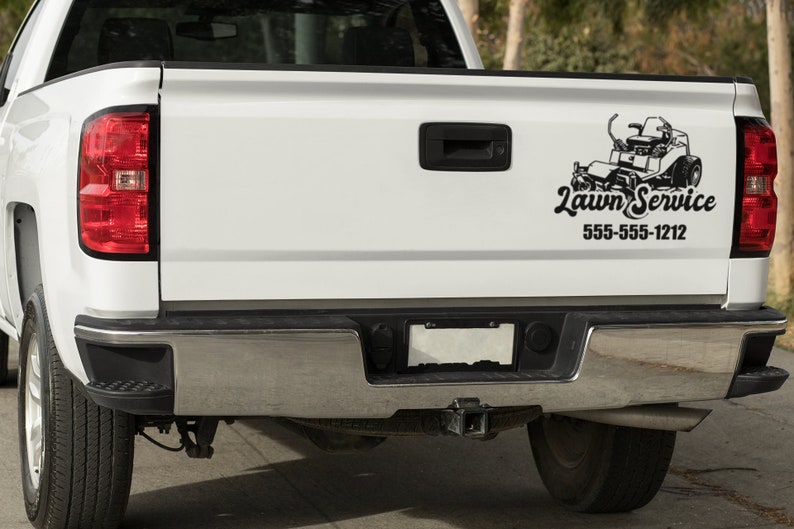 May include: White pickup truck with a black and white lawn service logo on the tailgate. The logo features a lawnmower and the text "Lawn Service" with the phone number 555-555-1212.