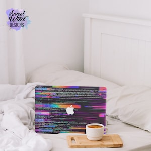 May include: A laptop computer with a colorful glitch effect design on the lid. The laptop is sitting on a white bed with a white blanket. A cup of coffee is on a wooden cutting board in front of the laptop.