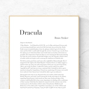 May include: A framed print of the novel "Dracula" by Bram Stoker. The text is black on a white background, with the title at the top. The frame is a light wood color, and the print is displayed on a white wall.