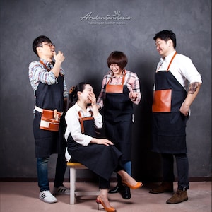 Puede incluir: Cuatro personas con delantales de mezclilla negros con detalles y bolsillos de cuero marrón. Los delantales tienen correas de cuero marrón. Los delantales se usan sobre varias camisas y jeans. Delantales de cuero hechos a mano.